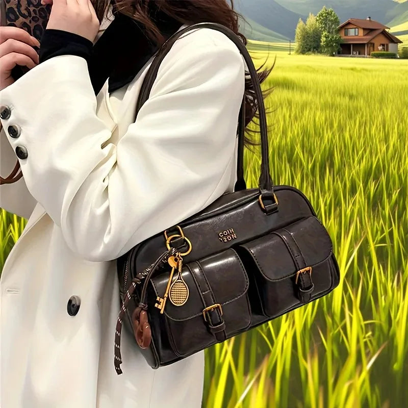 Person holding a black leather handbag with a scenic background of a house and green field.