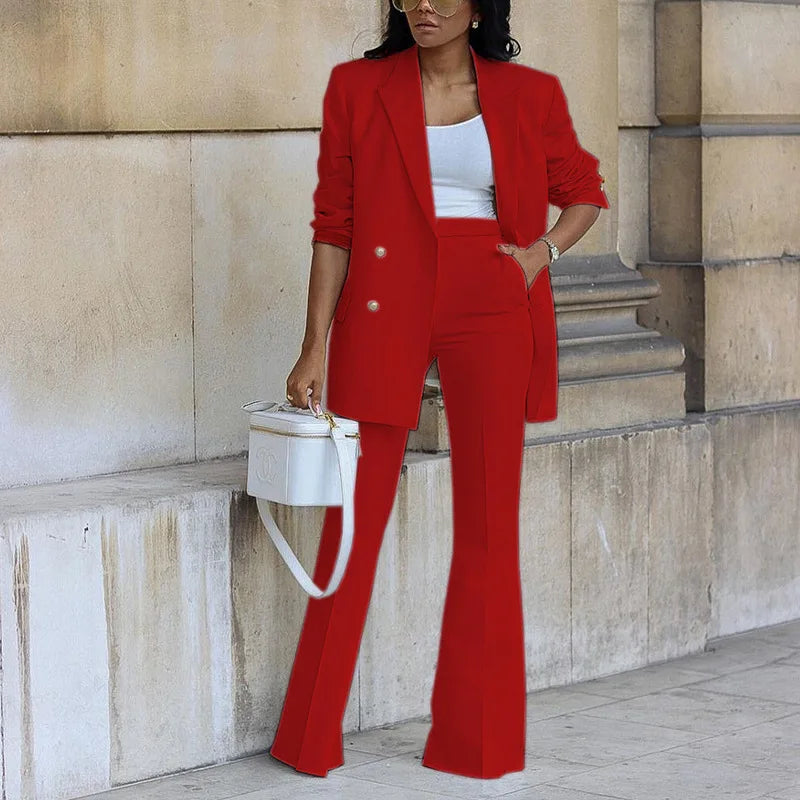 Woman in a red suit standing against a stone wall.