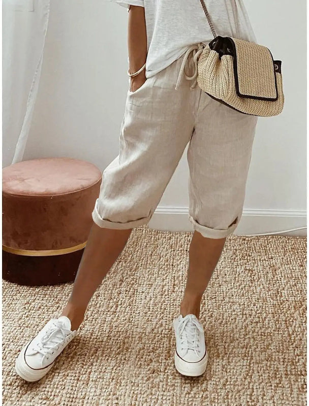 Person wearing beige shorts, white sneakers, and a straw bag on a carpeted floor.