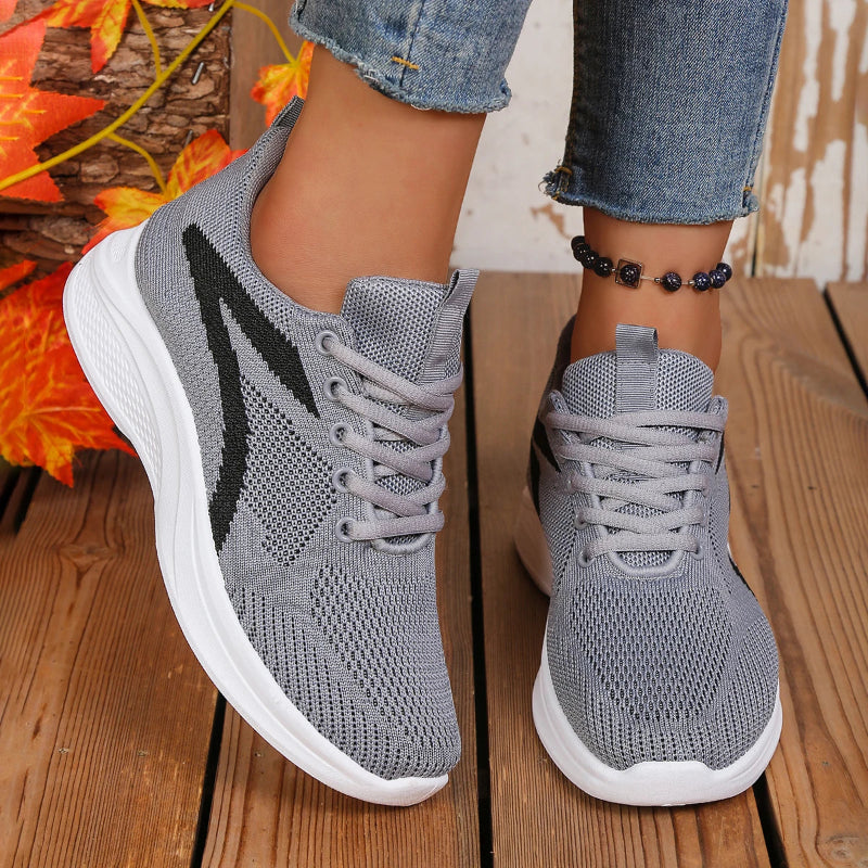 Gray sneakers with white soles worn on a wooden floor.