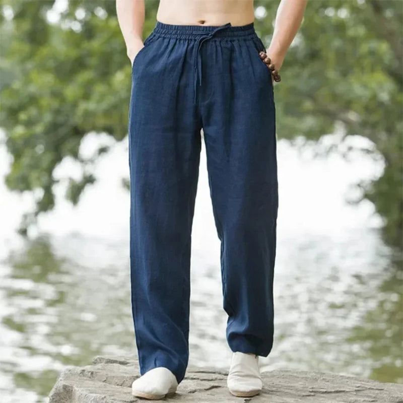 Person wearing navy blue pants standing by a body of water with greenery.