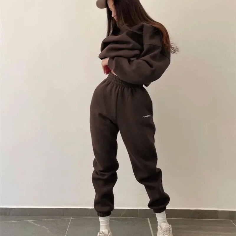 Person wearing a brown tracksuit with a logo on a plain background
