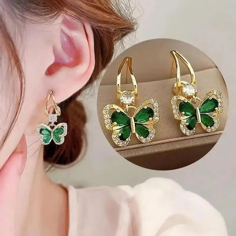Gold butterfly earrings with green gemstones worn by a person, close-up view.