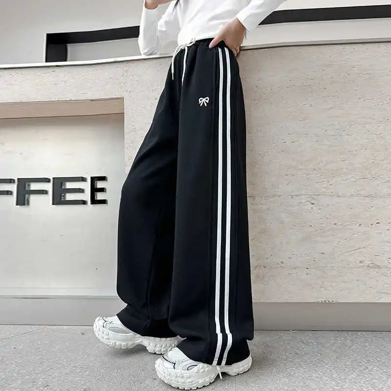 Person wearing black track pants with white stripes and a logo, standing in front of a 'COFFEE' sign.