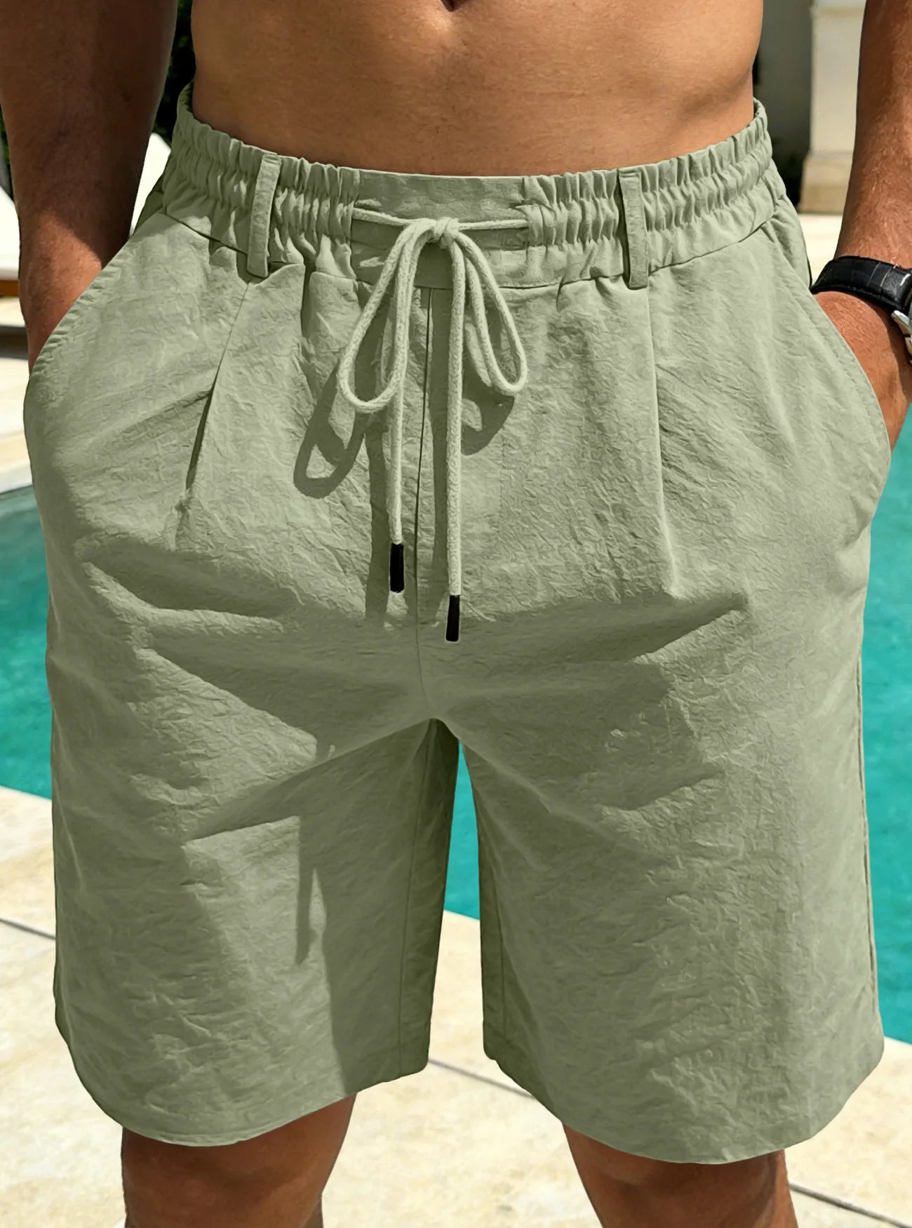Person wearing light green shorts with a drawstring in front of a pool.