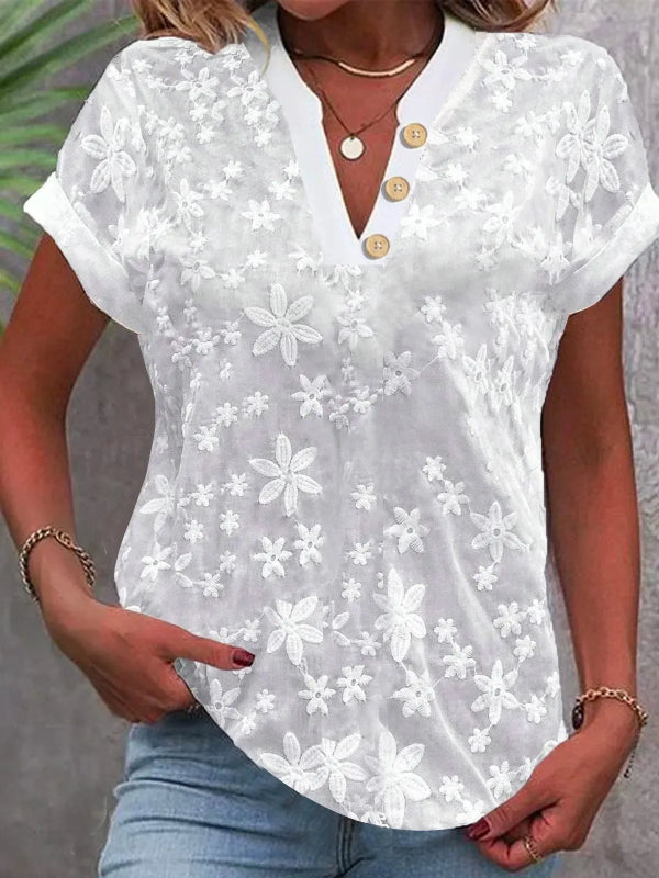 White floral lace blouse with gold buttons worn by a person against a neutral background