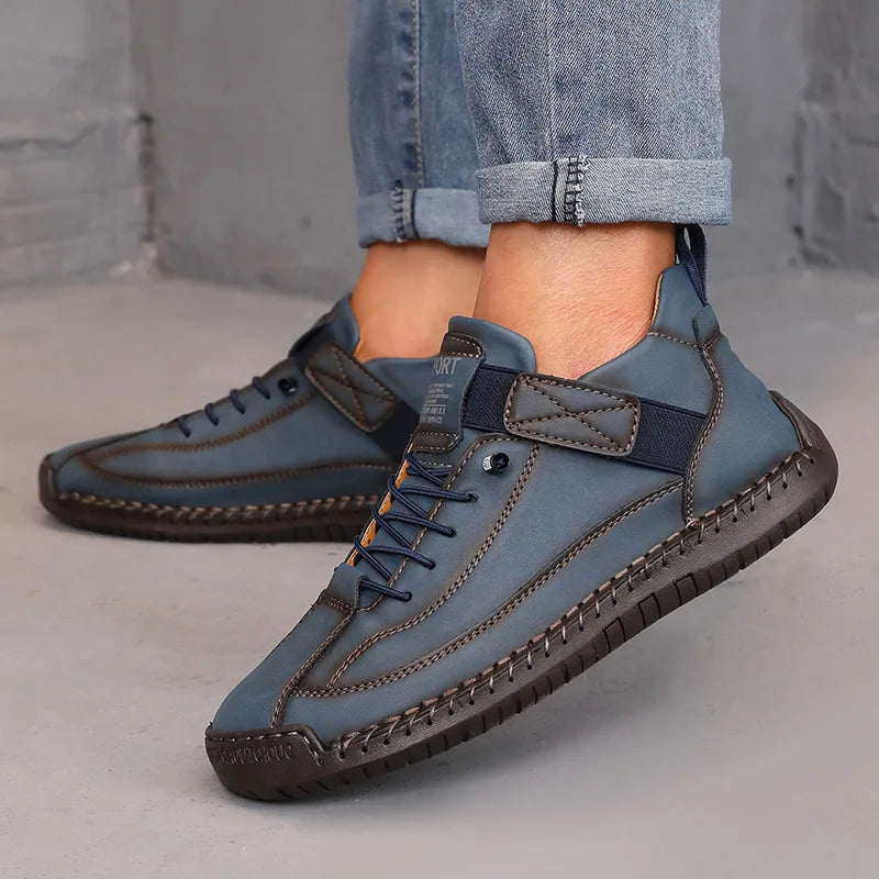 Blue leather shoes with brown accents worn by a person on a gray surface.