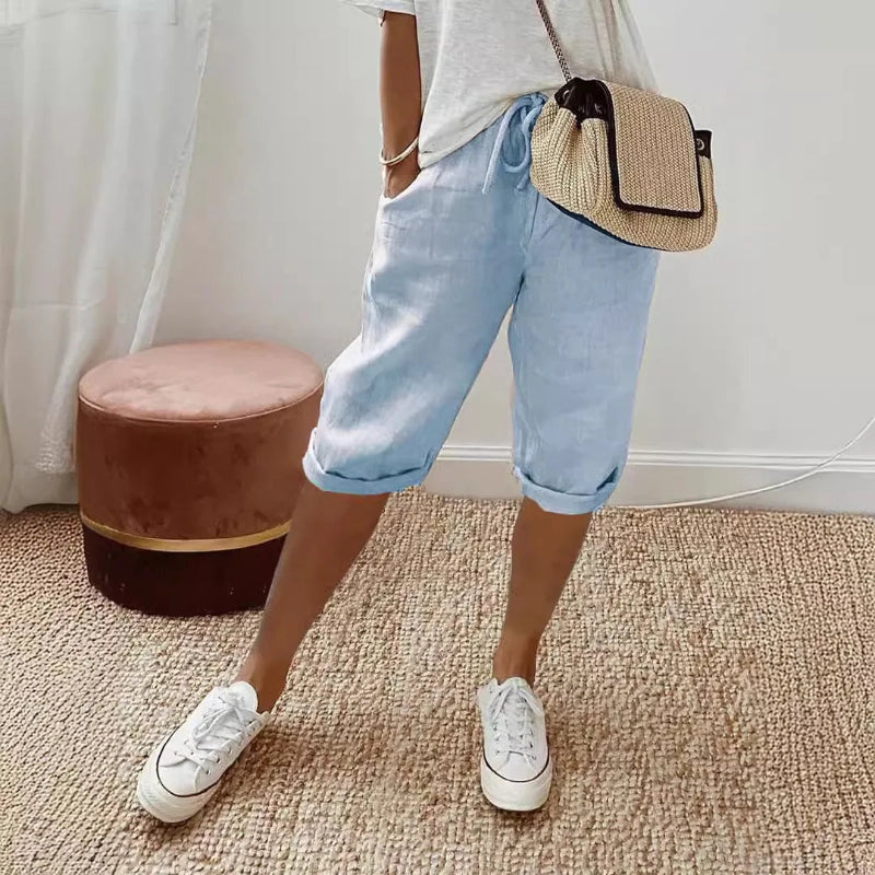 Person wearing light blue jeans, white sneakers, and a straw bag indoors.