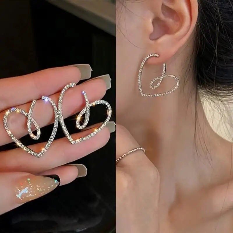 Heart-shaped earrings held in hand and worn on an ear.