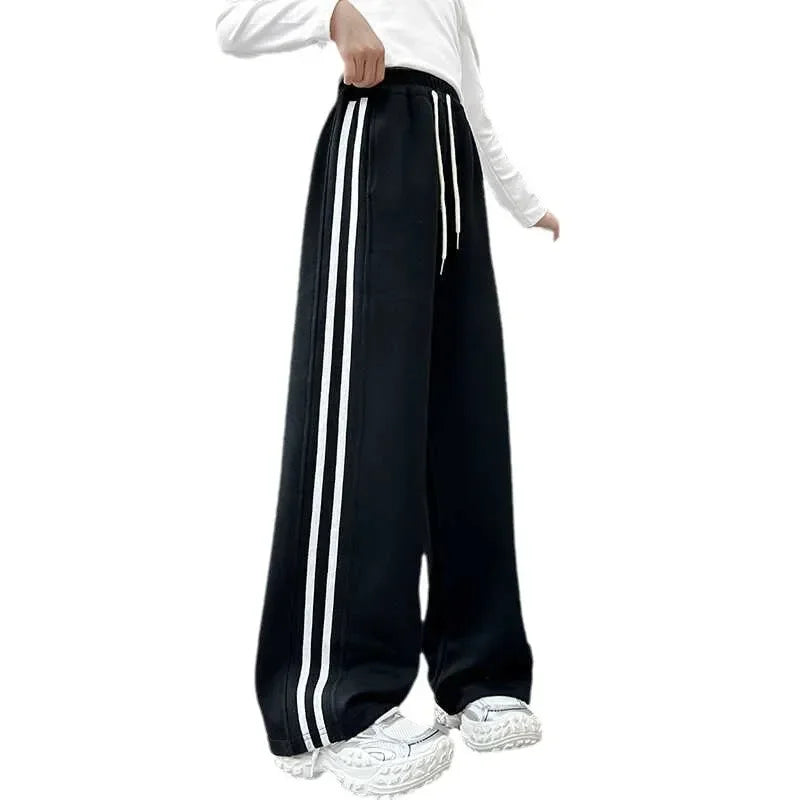 Black track pants with white stripes worn by a person on a white background