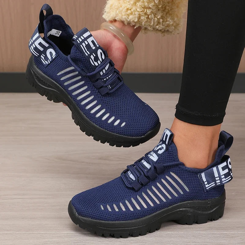 Person wearing blue athletic shoes with white stripes on a wooden floor.