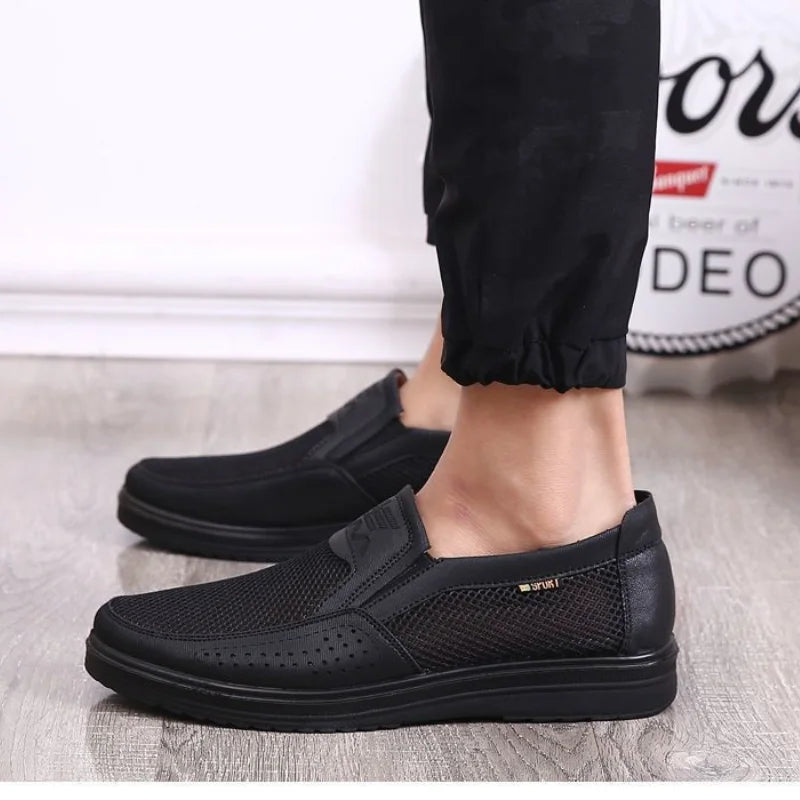 Black slip-on shoes worn with black pants on a light background