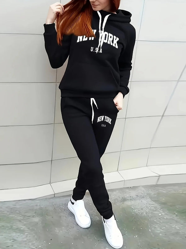 Person wearing a black 'New York USA' hoodie and pants against a light-colored wall.