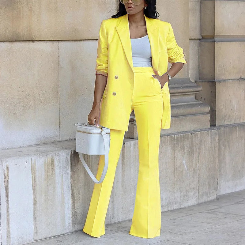 Woman in a bright yellow suit standing against a stone wall.