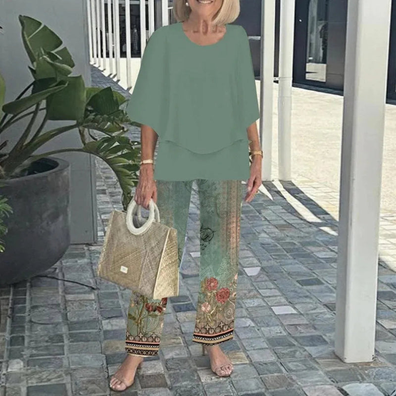 Woman in green outfit with floral pants holding a beige handbag outdoors.