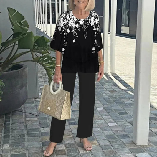 Woman in black outfit with white floral embroidery holding a beige handbag outdoors.