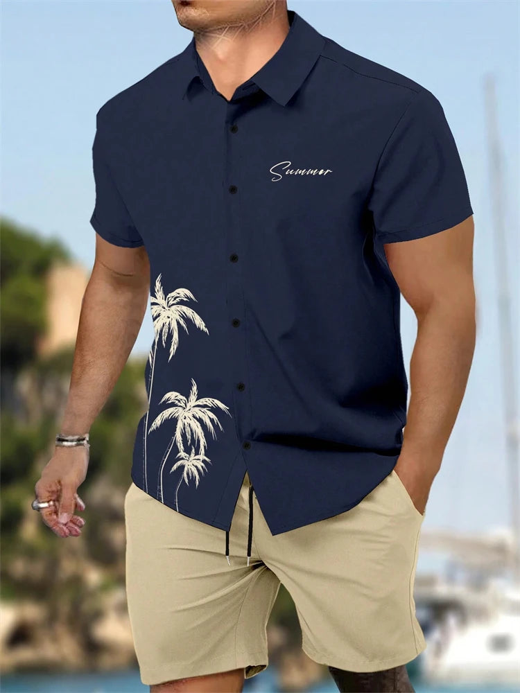 Man wearing a navy blue shirt with palm tree design and beige shorts, standing by a waterfront.
