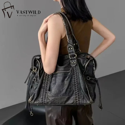 Person carrying a large black leather handbag with 'Vastwild' branding.