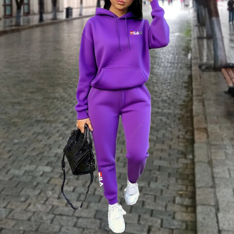 Person wearing a purple tracksuit with a brand logo, holding a black bag on a city street.