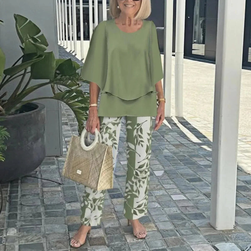 Woman in green outfit with floral pants holding a straw bag outdoors.