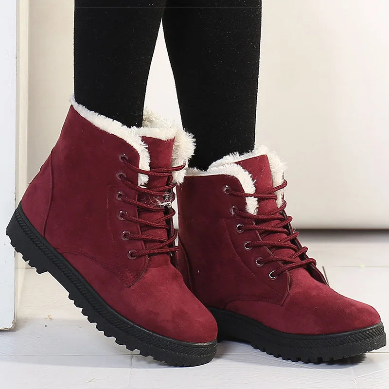 Red winter boots with white fur lining worn by a person on a light wooden floor.