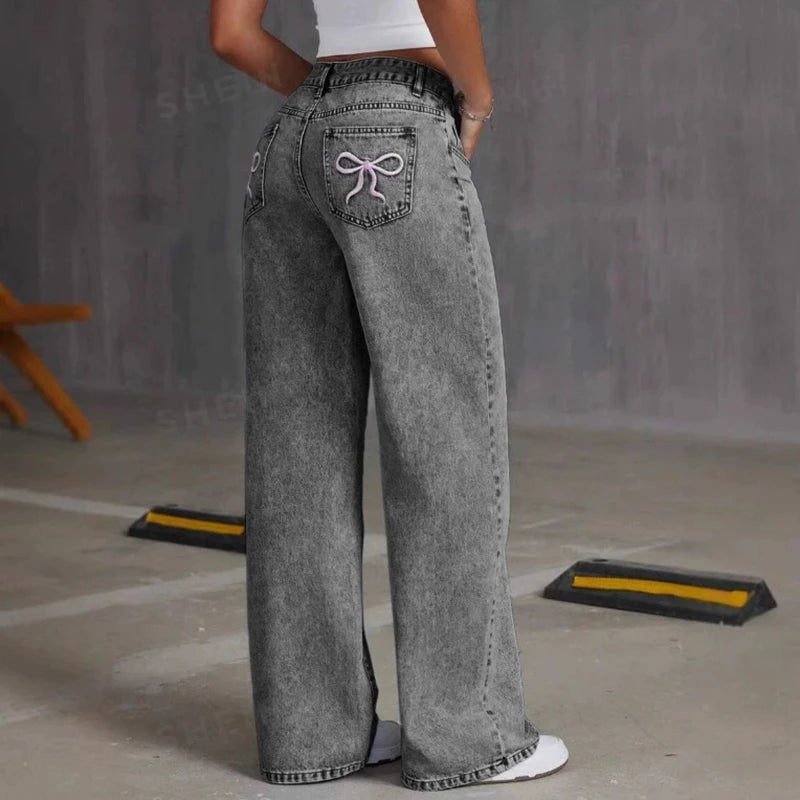 Person wearing gray wide-leg jeans with a decorative bow on the back pocket against a plain background.