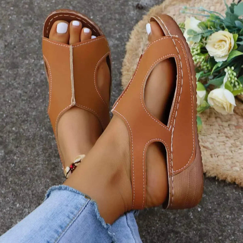 Brown open-toe sandals worn with light blue jeans on a textured surface.