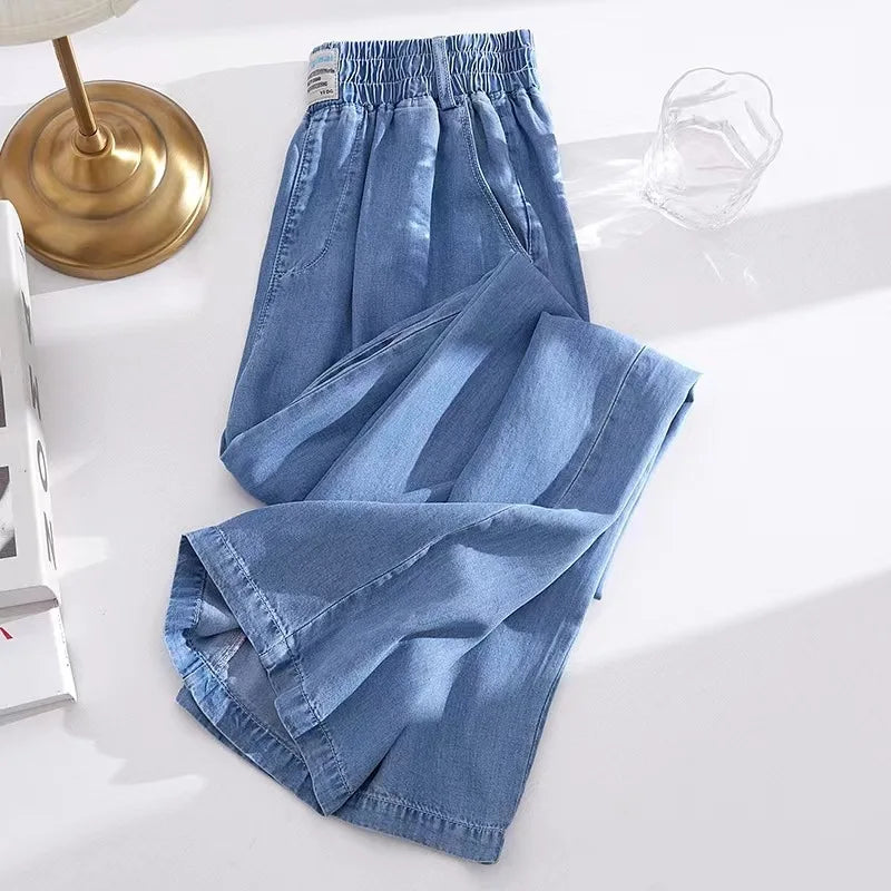 Blue denim pants on a white surface with a gold lamp and white decorative items in the background.