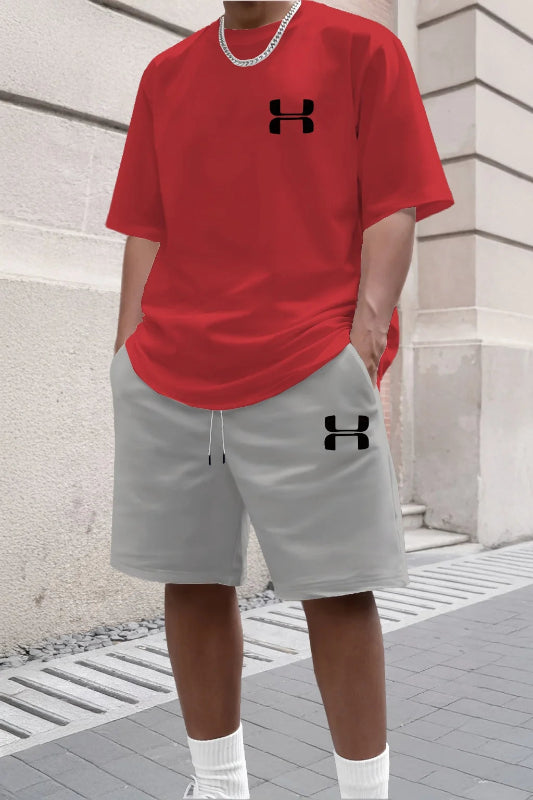 Person wearing a red t-shirt and gray shorts with Under Armour logos against a stone wall.