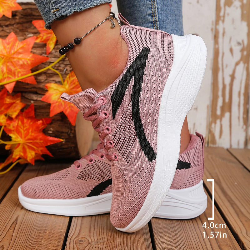 Pink and black athletic shoes on a wooden floor with autumn leaves in the background