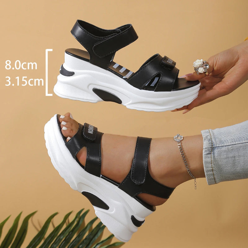 Black and white sandals with thick sole held by a hand, on a beige background.