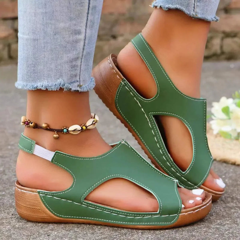 Green sandals with wooden soles worn by a person on a stone surface.