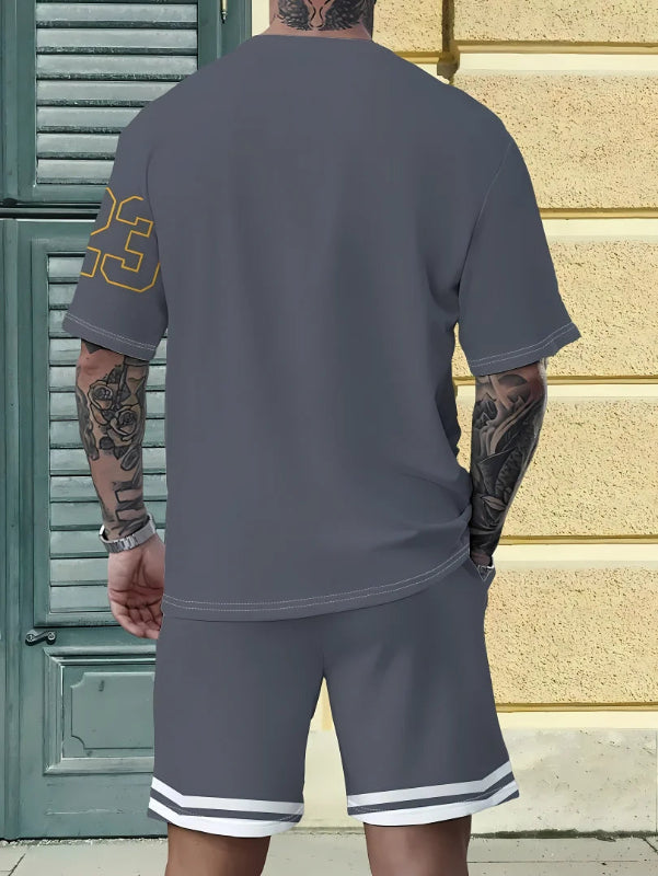 Person wearing a gray t-shirt and shorts set with tattoos visible, standing against a textured wall.