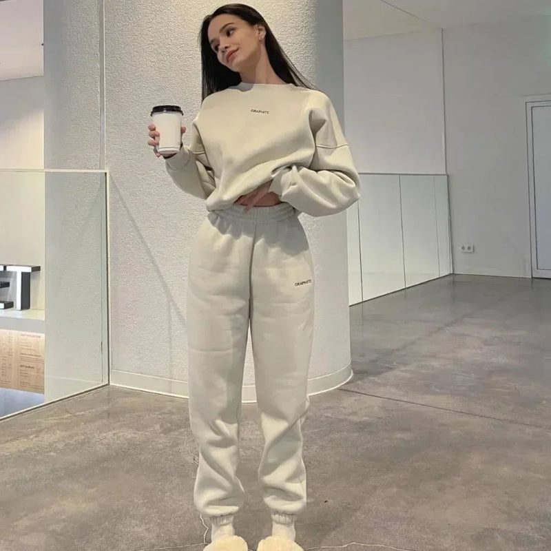 Woman in a beige tracksuit holding a coffee cup in a modern indoor setting