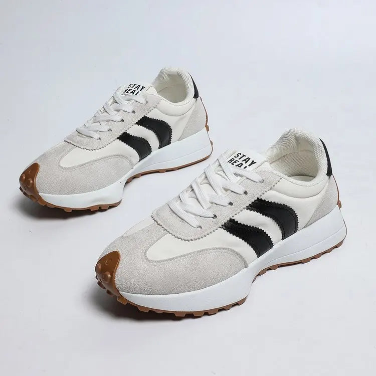 Pair of white sneakers with black stripes on a light gray background