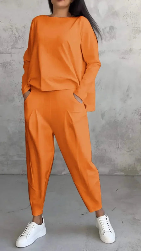 Person wearing an orange outfit with white sneakers against a gray concrete wall.
