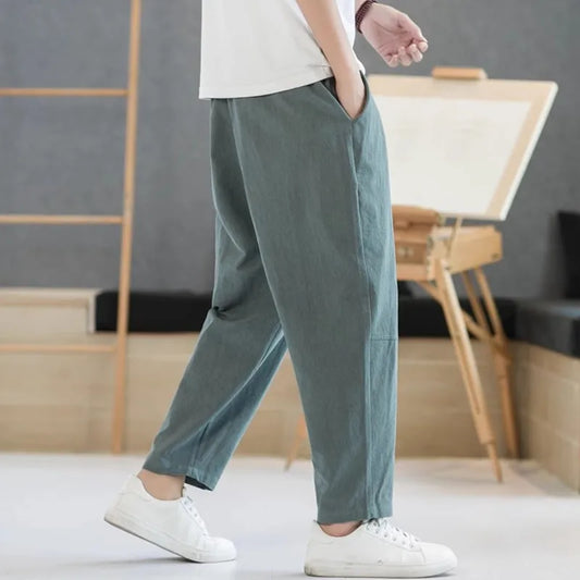 Person wearing green pants and white shoes in a room with wooden furniture and a gray wall.