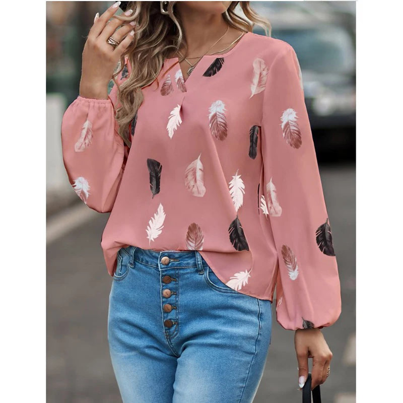 Person wearing a pink blouse with feather pattern and blue jeans outdoors.