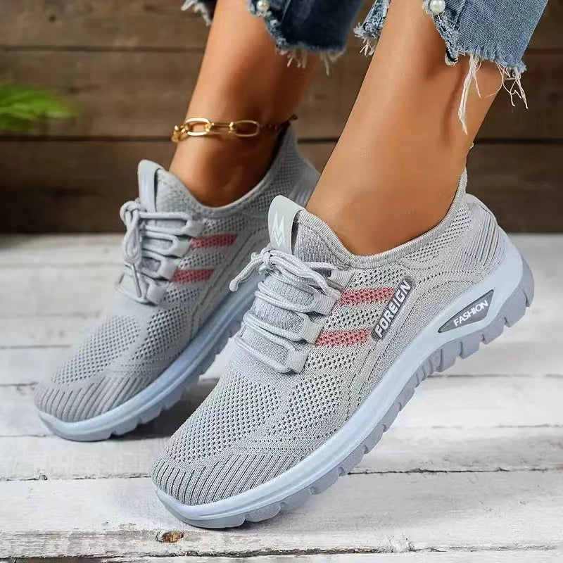 Gray sneakers with red accents worn by a person on a wooden floor.