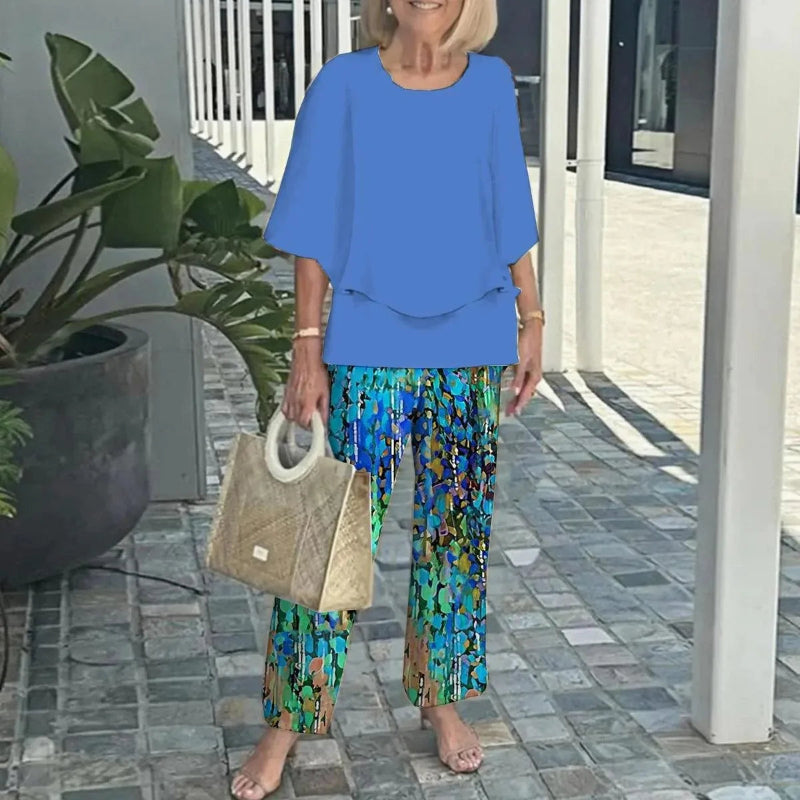 Woman in blue top and patterned pants holding a beige handbag on a patio.