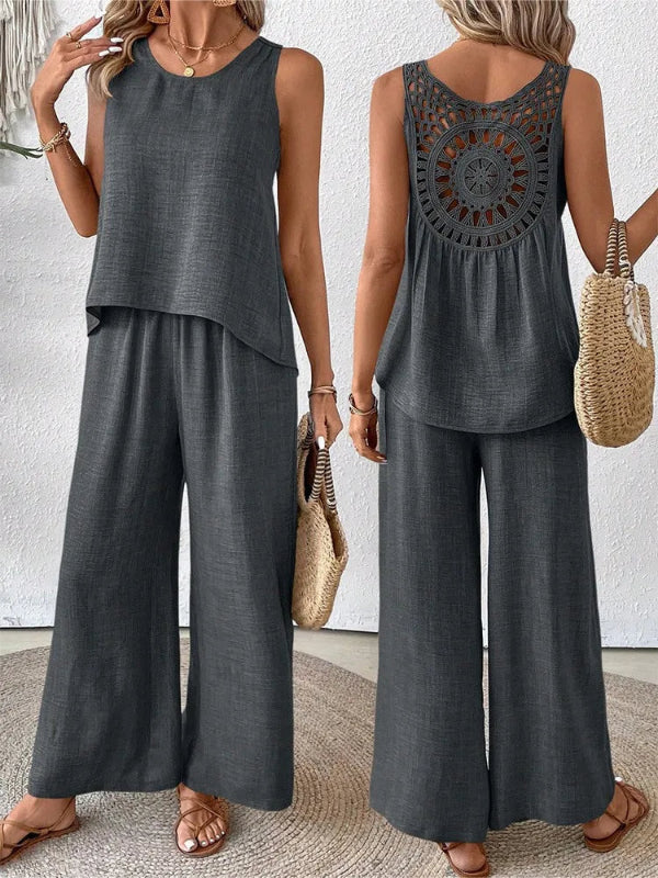 Woman wearing a gray sleeveless top and wide-leg pants, holding a straw bag.