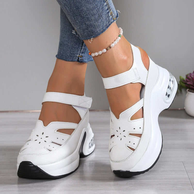 White platform sandals worn with blue jeans on a gray floor.