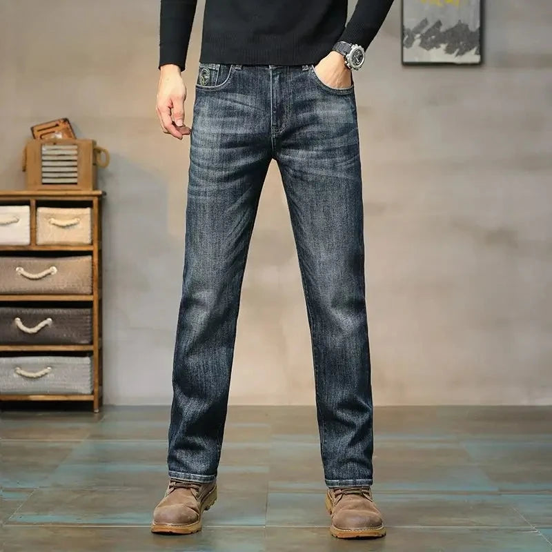 Person wearing blue jeans standing in a room with wooden furniture and a gray wall.