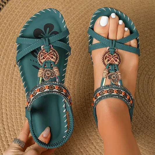 Teal sandals with decorative straps and charms on a textured brown surface