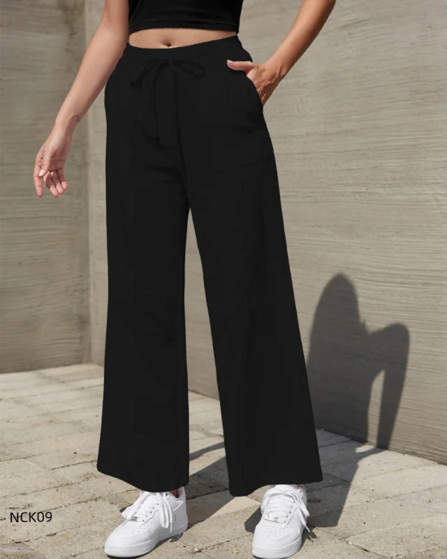 Person wearing black wide-leg pants and white sneakers against a neutral wall.
