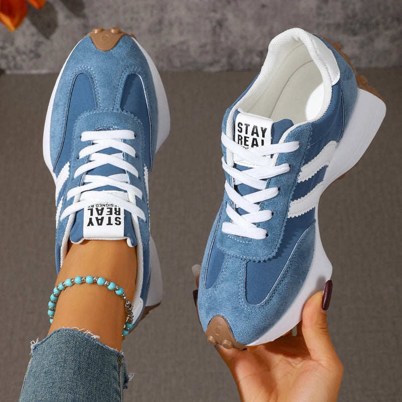 Blue sneakers with white soles held by a person against a neutral background