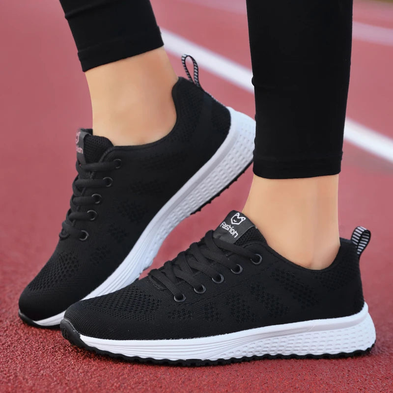 Black running shoes with white soles worn on a red track.