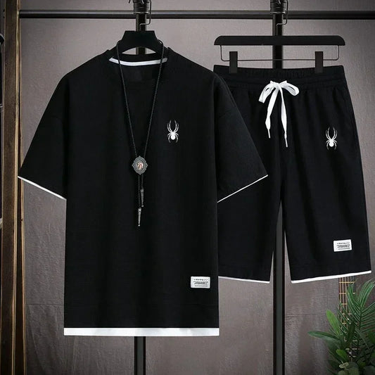 Black t-shirt and shorts set with spider design on hangers against a gray background.