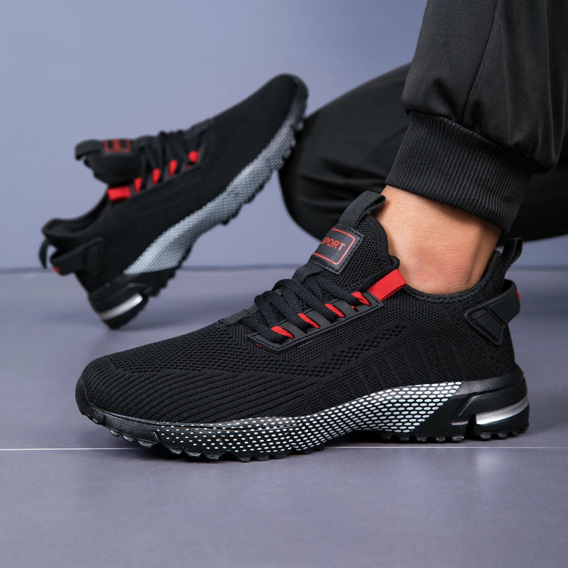 Black athletic shoes with red accents worn by a person on a gray background