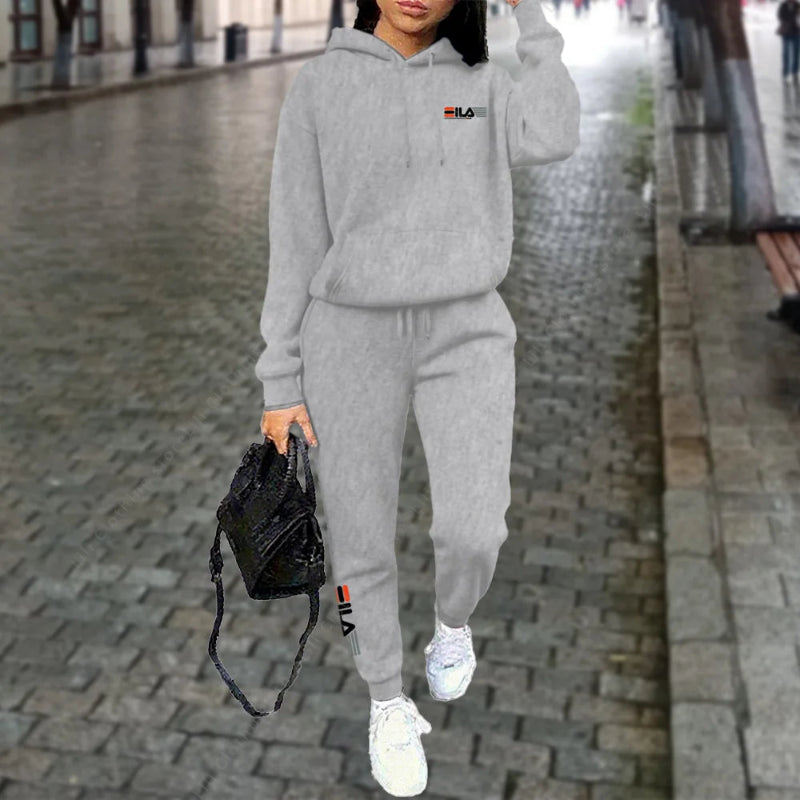 Person wearing a gray tracksuit with a brand logo on a city street.